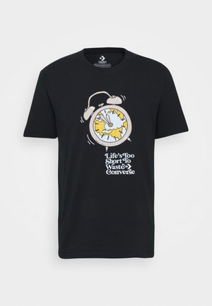 Schwarzes Baumwoll-T-Shirt mit einem cartoonhaften Design eines Weckers, runder Zifferblatt, gelben Akzenten und dem Text "Das Leben ist zu kurz, um Converse zu verschwenden."