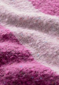 Wollstoff in verschiedenen Rosatönen mit einer strukturierten, flauschigen Oberfläche. Verfügt über gestickte Muster und subtile Sprenkel in Blau und anderen Farben.