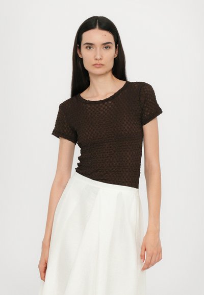 Bruine gestructureerde top met korte mouwen en een ronde halslijn, gecombineerd met een witte, geplooide, hoge taille rok. Eenvoudig ontwerp, lichte stof.