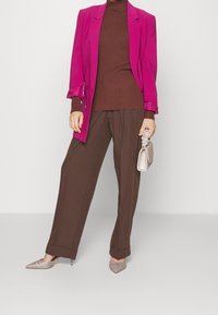 Blazer fucsia, suéter marrón acanalado y pantalones anchos marrones. Tacones plateados brillantes de punta y bolso metálico pequeño.