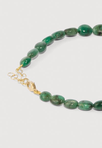 Collana di pietra verde con perle ovali, caratterizzata da leggere variazioni di texture. La minuteria e la chiusura in oro offrono un accento contrastante.