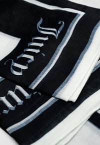 Foulard a motivi black and white con testo elegante, caratterizzato da strisce alternate di ampiezze variabili e una texture morbida e leggera.