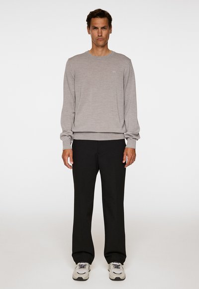 Vaaleanharmaa neulepaita pyöreällä pääntiellä, yhdistetty mustiin väljiin housuihin ja harmaisiin lenkkareihin. Yksinkertainen muotoilu ilman kuvioita.