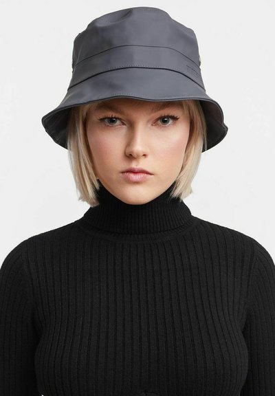 Grau wasserdichter Hut mit breiter Krempe, der eine glatte Textur und subtile Nahtdetails aufweist, getragen über einem schwarzen gerippten Rollkragenpullover.