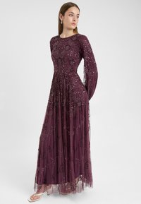 Abito lungo bordeaux con maniche lunghe, caratterizzato da dettagli intricate di perline e ricami floreali, tessuto trasparente a strati e una silhouette fluida.
