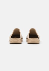 Beiga slip-on skor i ett slätt, glänsande material, med låg baksida och en strukturerad gummisula med ett zigzagmönster.