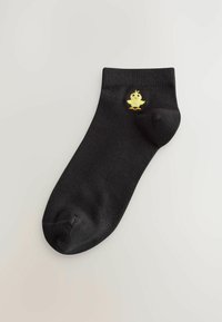 Crne čarape do gležnjeva izrađene od mekanog materijala, s malim izvezenim žutim pićem na vanjskoj strani.