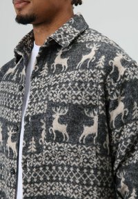 Chemise en laine grise avec un motif de renne crème, dotée d'un col, d'une fermeture à boutons et d'une poche poitrine. Design texturé et chaud.