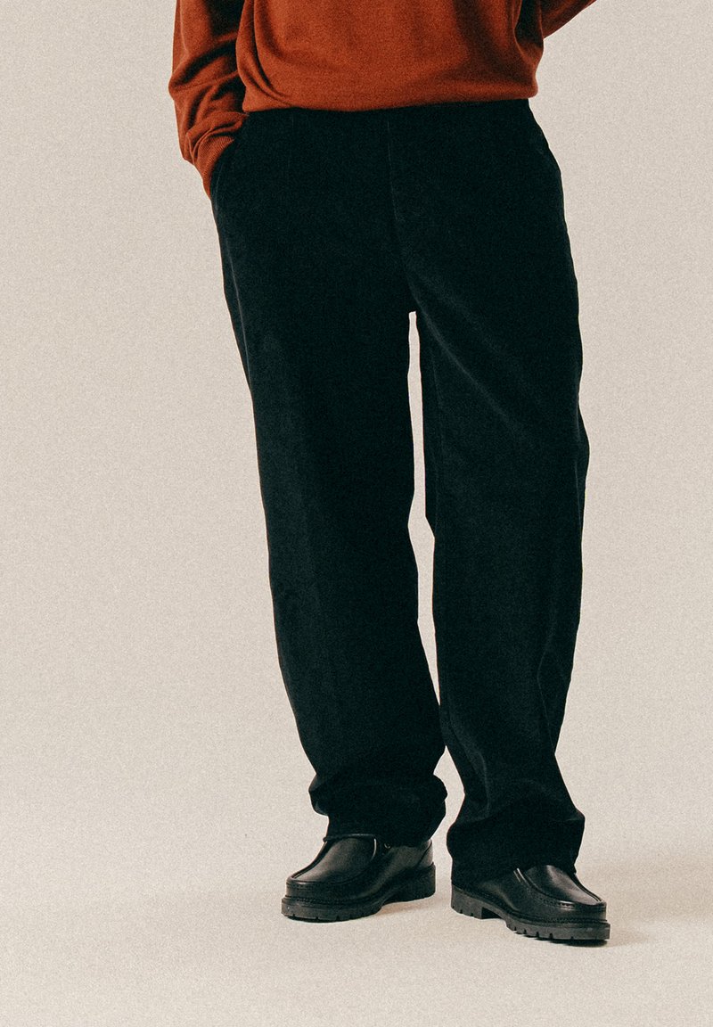 Μαύρο παντελόνι καστόρι με χαλαρή γραμμή και πλαϊνές τσέπες, συνδυασμένο με μαύρα δερμάτινα παπούτσια με χοντρή σόλα.