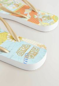 Värvilised plätud tekstureeritud vahtpohjaga, millel on erksad mustrid, mis sisaldavad kuldseid detaile ja heledaid tan värvi rihmasid.