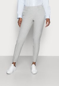 Pantalons gris clair avec une texture lisse, coupe ajustée et taille élastique. Portés avec des baskets blanches.