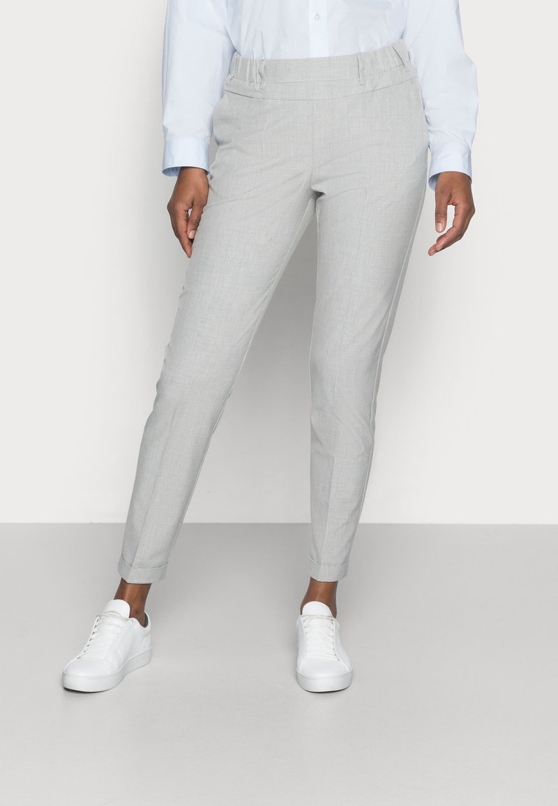 Pantalons gris clair avec une texture lisse, coupe ajustée et taille élastique. Portés avec des baskets blanches.