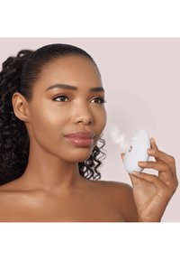 Vapeur facial portable blanche en forme arrondie avec un petit bouton, émettant une fine brume. Texture lisse sur un fond rose clair.