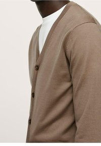 Cárdigan de punto marrón con escote en V y cinco botones, que presenta un tejido texturizado y una silueta suave. Llevado sobre una camisa blanca.