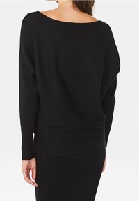 Pull noir côtelé avec un large décolleté bateau, coupe ample et manches longues. Le matériau présente une finition texturée et un design décontracté.