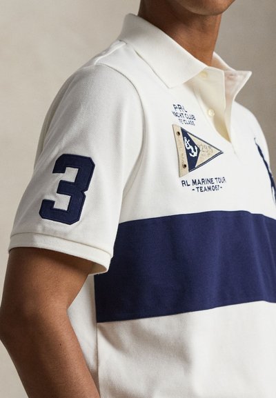 Λευκό και ναυτικό polo πουκάμισο με μεγάλο αριθμό 3 στο μανίκι, εξάρτημα με ναυτική σημαία και κείμενο «RL Marine Tour - Team 067» στο στήθος.