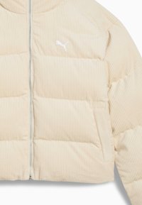 Beige puffjacka med ribbad textur, med dragkedja fram och vitt Puma-logotyp på vänster bröst, designad med en kortad silhuett.
