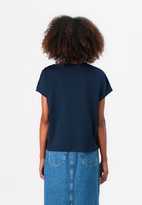 Marineblå kortermet topp med en avslappet passform, med rund halslinje og knappdetaljer på skuldrene, sammen med et denimskjørt.