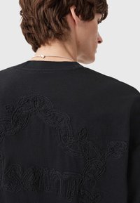 Sort sweatshirt med et tekstureret kædedesign broderet på ryggen. Rund hals og blødt stof med diskrete syningsdetaljer.