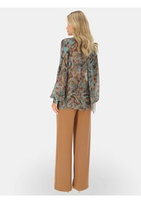 Przezroczysta bluzka w wzór paisley w odcieniach teal, brązu i pomarańczy, z szerokimi rękawami. Zestawiona z brązowymi spodniami o wysokim stanie i luźnym kroju.
