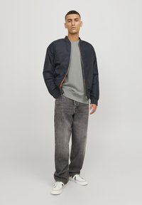 Chaqueta bomber navy con cremalleras naranjas sobre un sudadera gris, combinada con jeans gris de corte holgado y zapatillas blancas con acentos negros.
