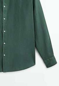 Chemise boutonnée à manches longues de couleur vert foncé avec des boutons blancs, montrant le devant et la manche droite sur un fond uni.