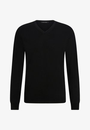 Maglione nero a scollo a V in tessuto a maglia, abbinato a pantaloni della tuta a sigaretta grigi chiari. Il modello indossa sneaker bianche, con le mani in tasca.