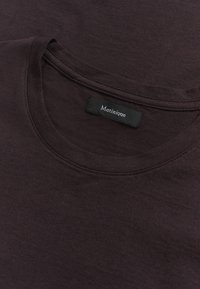 Camiseta de cuello redondo en púrpura oscuro, hecha de una tela suave con una textura lisa. Presenta una etiqueta con "Matinique" en texto blanco sobre un fondo negro.