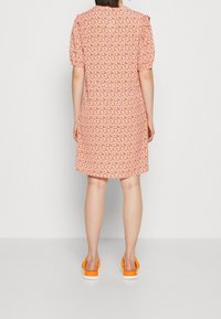 Abito rosa a maniche corte con motivo floreale, lunghezza al ginocchio, taglio leggermente svasato, indossato con sandali arancioni. Tessuto dalla texture liscia.