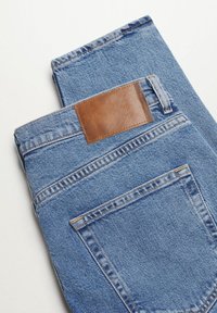 Jean en denim bleu plié avec une poche arrière visible et un patch de marque en cuir marron sur la ceinture.