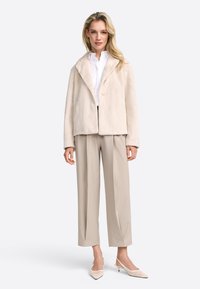 Veste en fausse fourrure crème avec un col châle, fermeture à un bouton, associée à un pantalon beige ajusté. Texture lisse, coupe décontractée.
