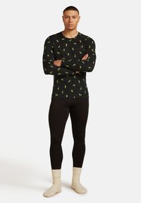 Zwarte longsleeve shirt met groene patronen, gecombineerd met zwarte leggings en crèmekleurige, geribbelde sokken. Passende ontwerp, gladde textuur.