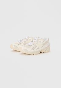 Des chaussures de sport légères en mesh crème avec des accents blancs, dotées d'un col rembourré, d'un devant à lacets et d'une semelle en caoutchouc texturé.