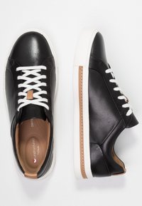 Baskets en cuir noir avec des lacets blancs, des accents beige et une semelle en caoutchouc blanche. Design élégant avec un bout arrondi et une texture lisse.