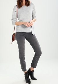 Szary sweter z dzianiny z przyciskami po bokach, w połączeniu z szarymi spodniami jeansowymi z mankietami. Czarne botki na obcasie do kostek dopełniają całość.