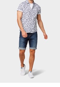 Valkoinen lyhythihainen nappipaita, jossa on laivaston sinisiä palmuprinttejä, yhdistettynä käännettyihin farkkushortseihin ja valkoisiin tennareihin. Yksinkertainen ja rento muotoilu.