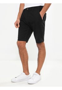 Bermudas de algodón negro con corte recto, bolsillos frontales y cierre de botón. Combinadas con zapatillas blancas para un look contrastante.
