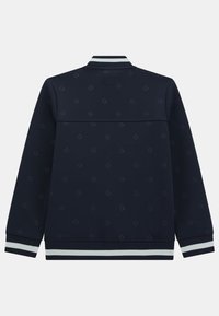 Temno-modra dukserica z ribastim ovratnikom in manšetami, ki prikazuje subtilen vzorec logotipa. Gladka textura in kontrastne bele črte na robu.