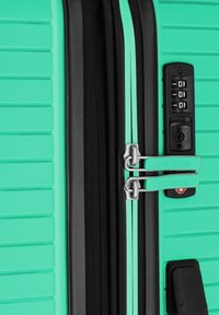 Maleta rígida en color teal con textura acanalada, cremalleras negras, cerraduras de cable duales y una cerradura aprobada por la TSA para un viaje seguro.