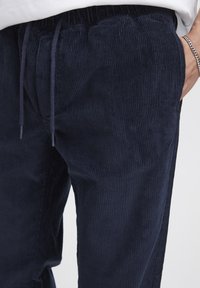 Navy corduroy joggers with a drawstring waist, featuring vertical ribbing and side pockets for added comfort and functionality.