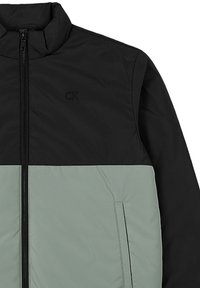 Giacca zip-up nera e grigia con colletto alto e discreto logo "CK" nella zona superiore nera del petto.
