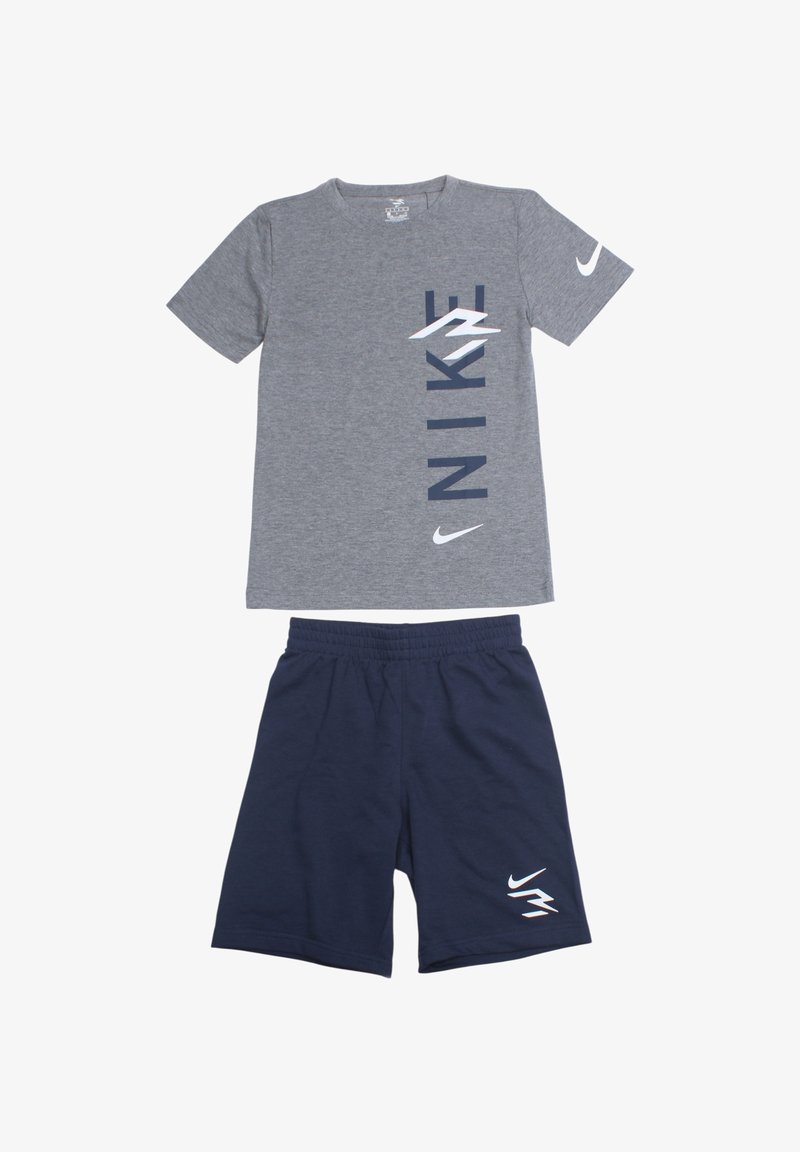 T-shirt en coton gris avec impression verticale "NIKE" en bleu marine et logo blanc ; assorti à un short bleu marine, taille élastique et détail logo blanc.