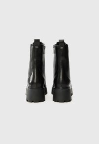 Bottines en cuir noir avec une semelle épaisse, comportant des fermetures éclair sur les côtés et des tirants en tissu en boucle à l'arrière. Texture lisse, design moderne.