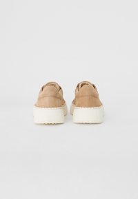 Beige suede sneakers with a thick white sole, featuring stitched detailing along the sides and a low-profile design for easy wear.