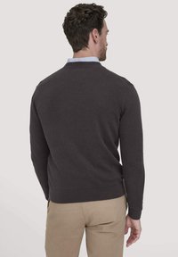 Donkergrijze pullovertrui met een geribde kraag en manchetten, met een gladde breistekstuur. De achterkant toont een aansluitend ontwerp met een lichte tapering.