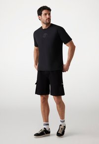 Sort crew neck t-shirt med et diskret logo, parret med sorte cargo shorts med sidelommer og en mærkeaccent. Sneakers med snørebånd.