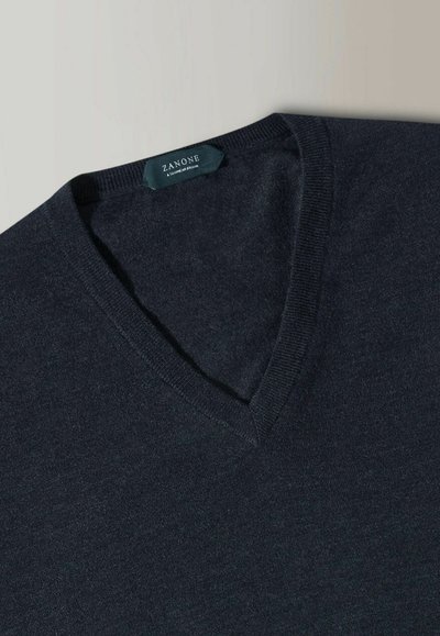 Dunkelblauer V-Ausschnitt-Pullover aus weichem Stoff, mit geripptem Kragen und minimalistischem Design, das ein Etikett mit dem Markennamen zeigt.