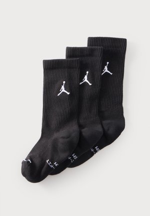 Trzy pary czarnych skarpetek do kostki z białymi logo Jumpman ułożone na jasnym tle.