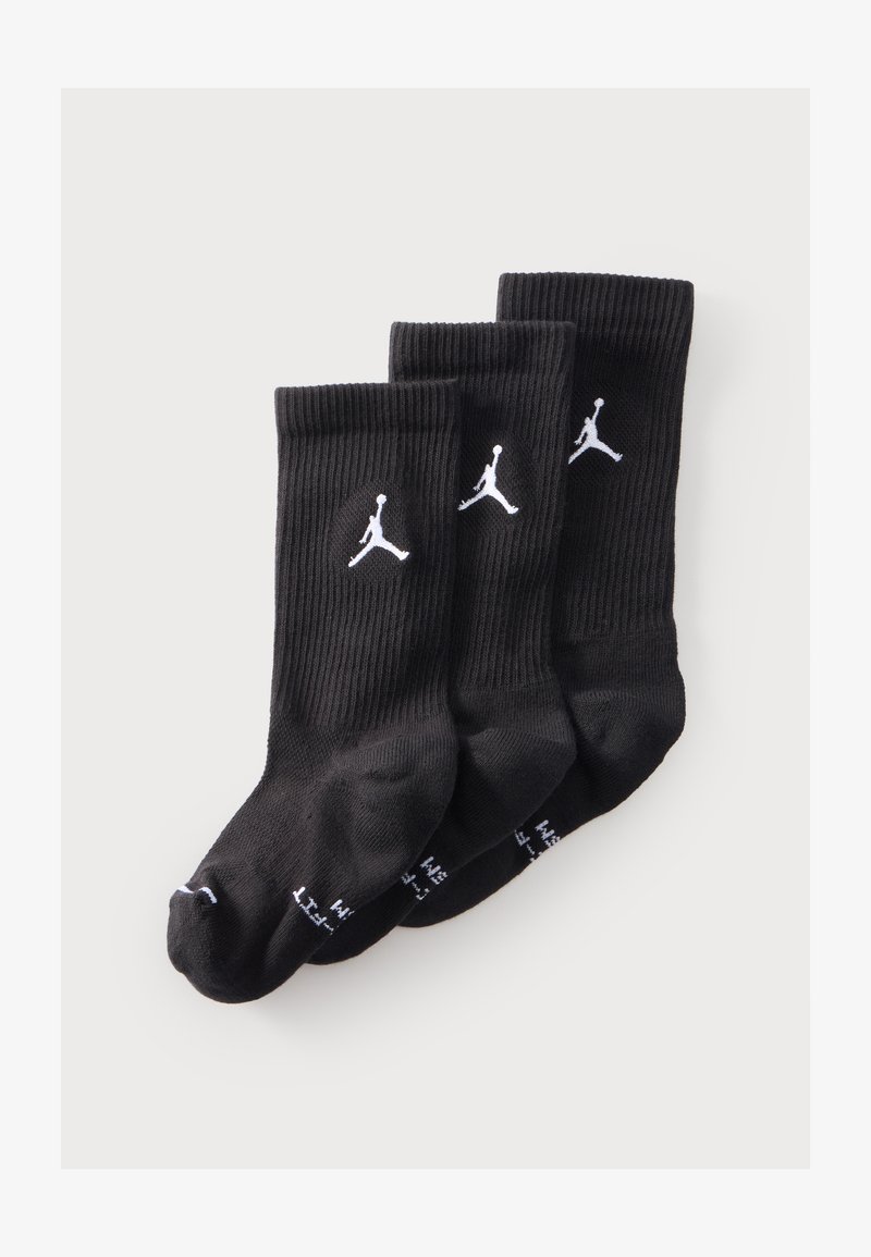 Trois paires de chaussettes noires montantes avec logos Jumpman blancs empilées sur un fond clair.