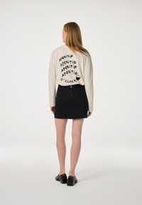 Crèmekleurig shirt met lange mouwen en zwarte tekstontwerp, gecombineerd met een zwarte minirok met een rits aan de achterkant en platte zwarte schoenen.